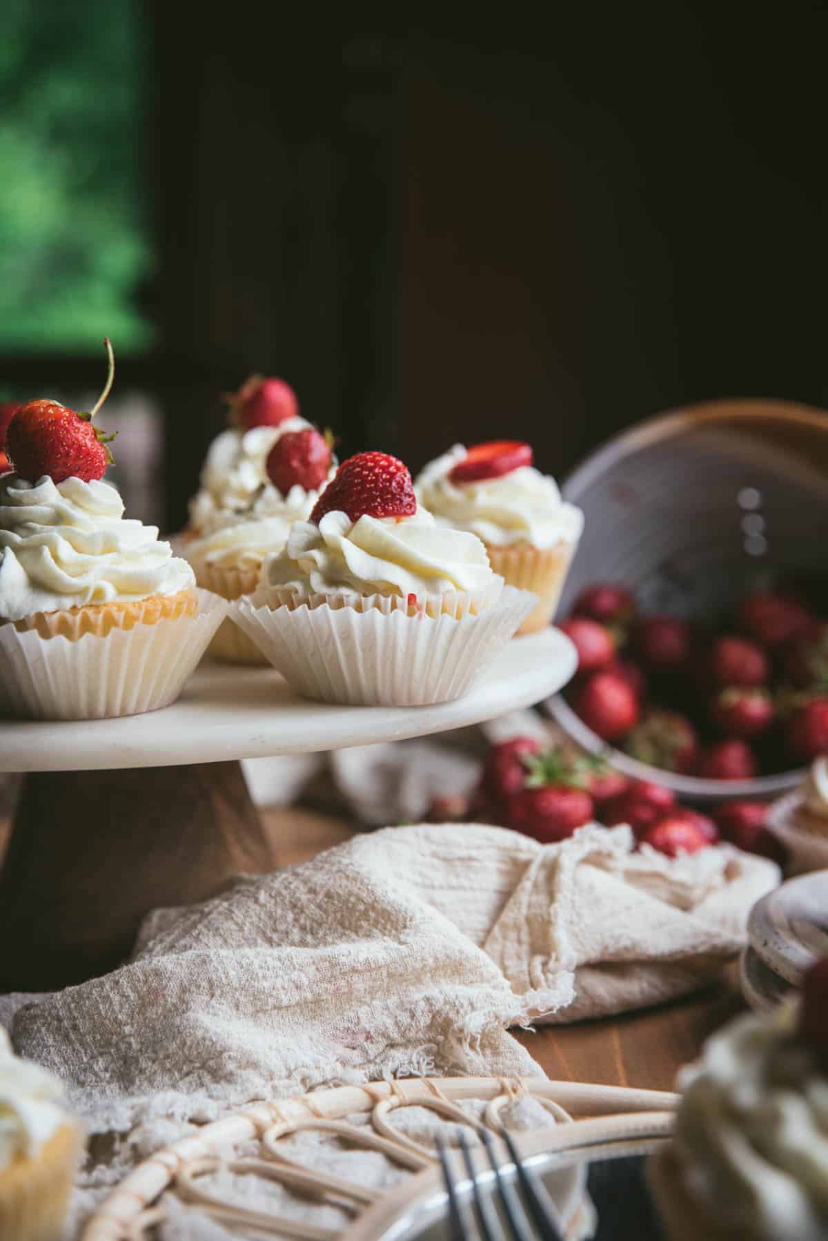 strawberry topped cupcakes on a cake stand with fresh strawberries in the background