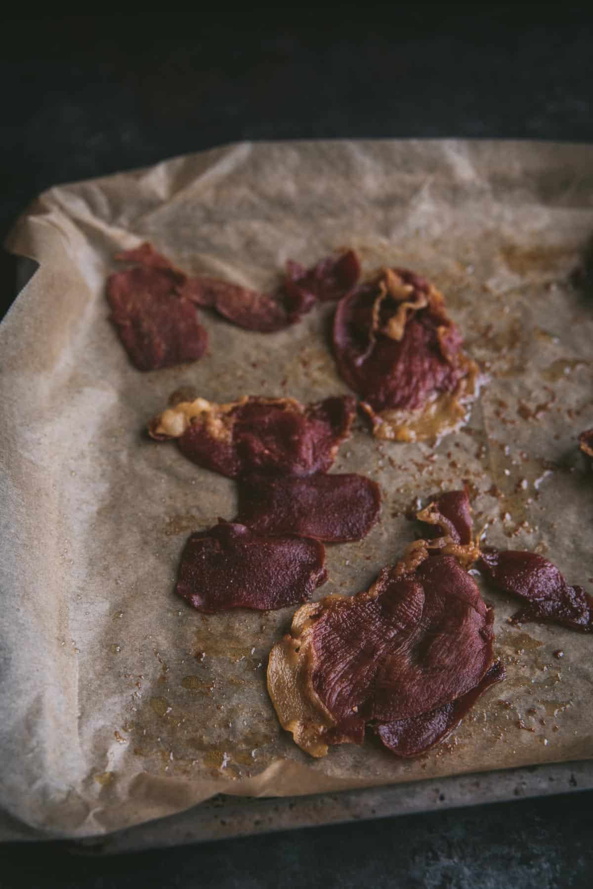 Baking sheet topped with parchment paper containing cooked prosciutto.