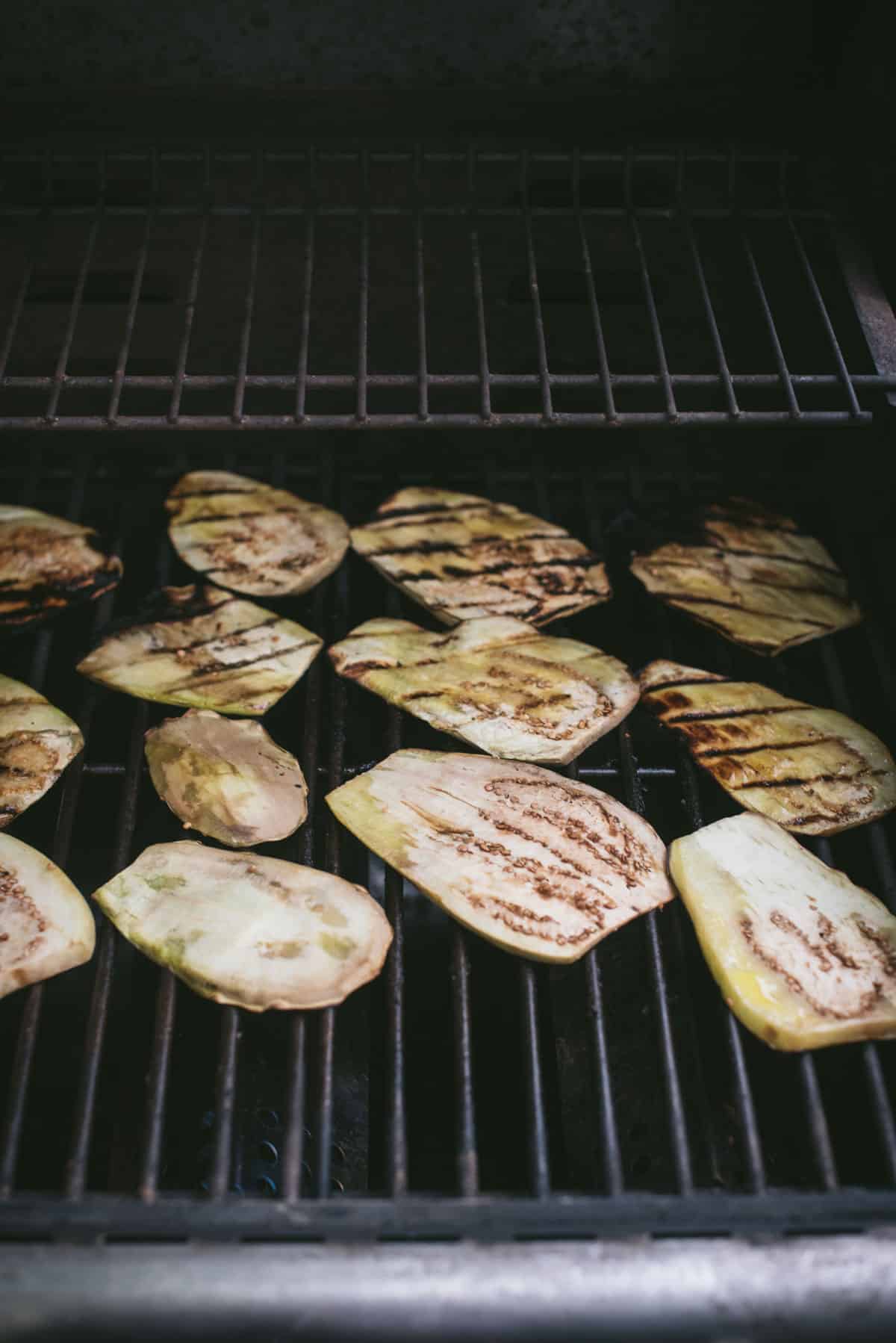The eggplant slices are sitting on a bare grill to cook. They are nicely spread out and they look nearly finished. There is beautiful charred lines across the eggplant.
