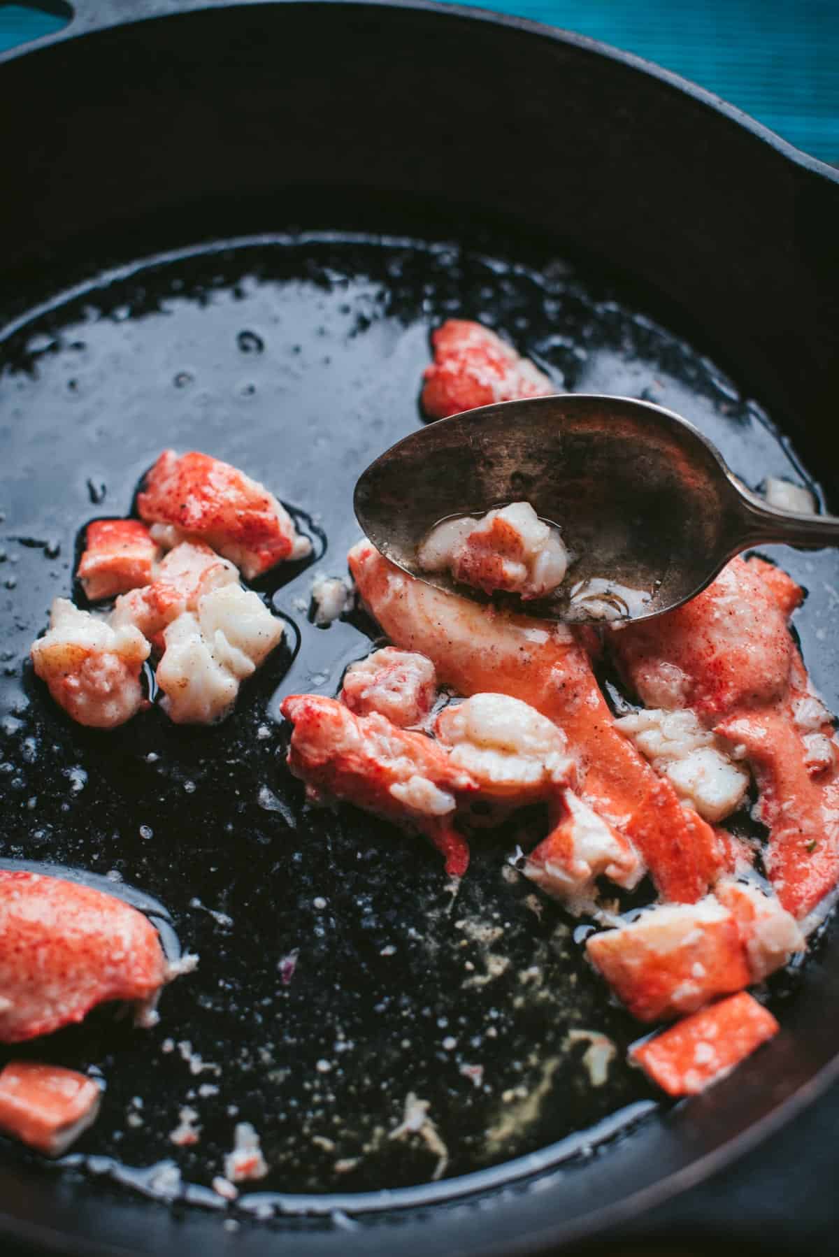 Lobster tails simmering in butter in a black saucepan.