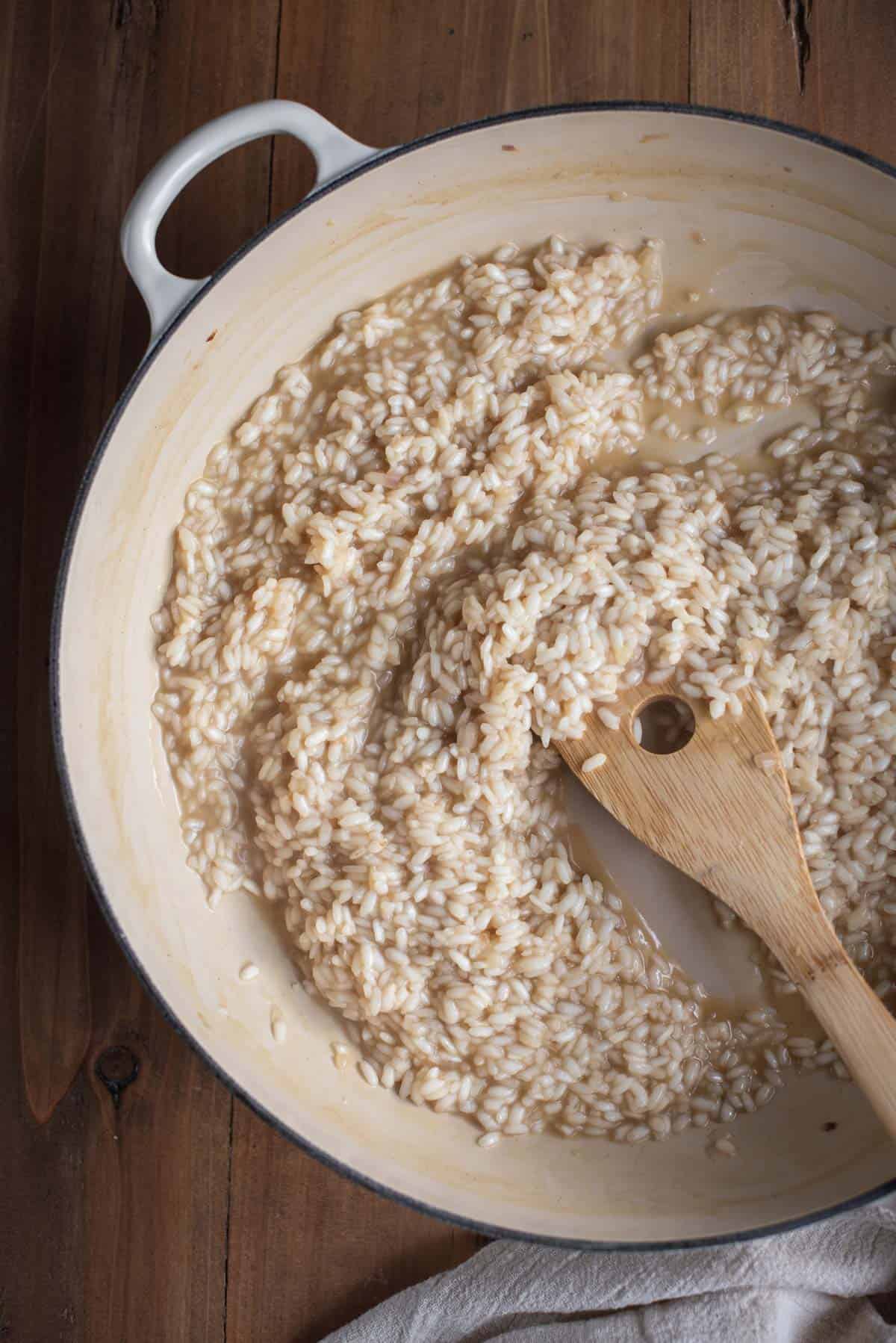 Rice cooked further in a white skillet with a wooden spoon stirring the mixture.