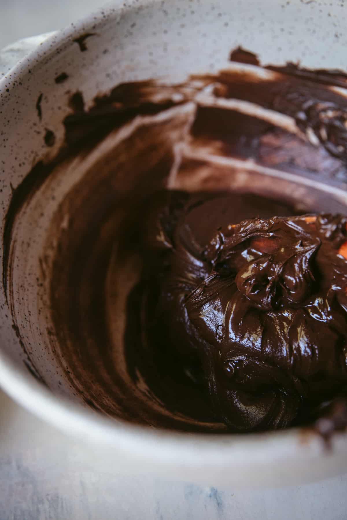 Melted chocolate and butter in a ceramic mixing bowl with a spatula scooping it from the side.  Chocolate residue is smeared on the sides.