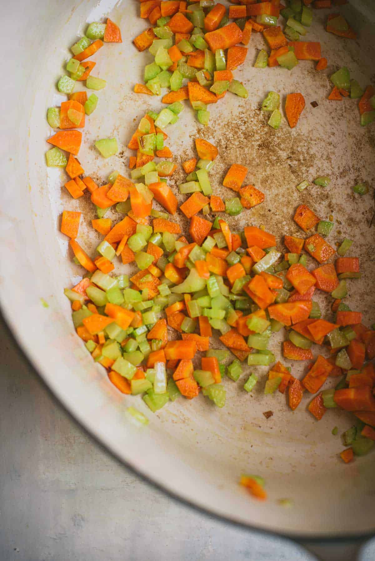 Carrots and celery are being cooked in the bottom of a large white saucepan.