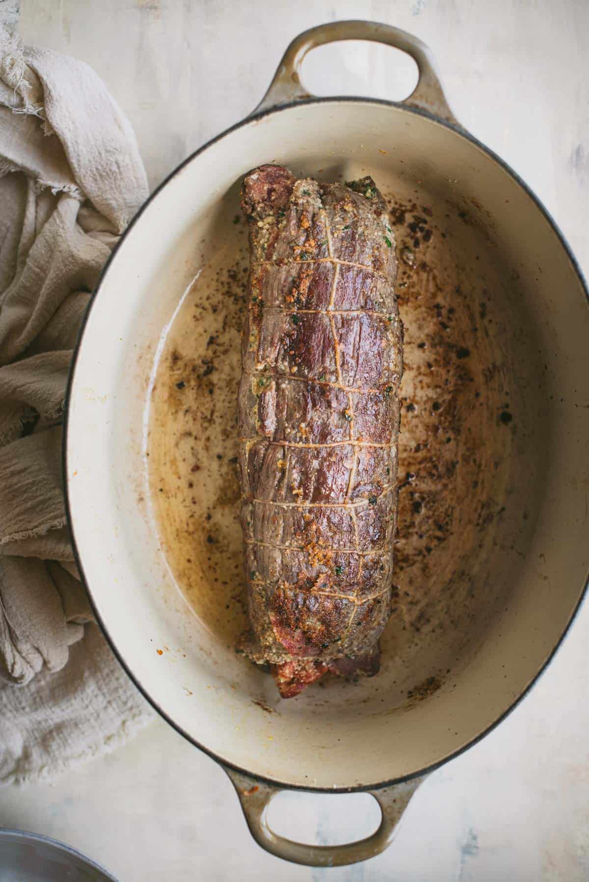 The vegetables have been removed from the large white saucepan and the beef braciole has been placed inside to braise.