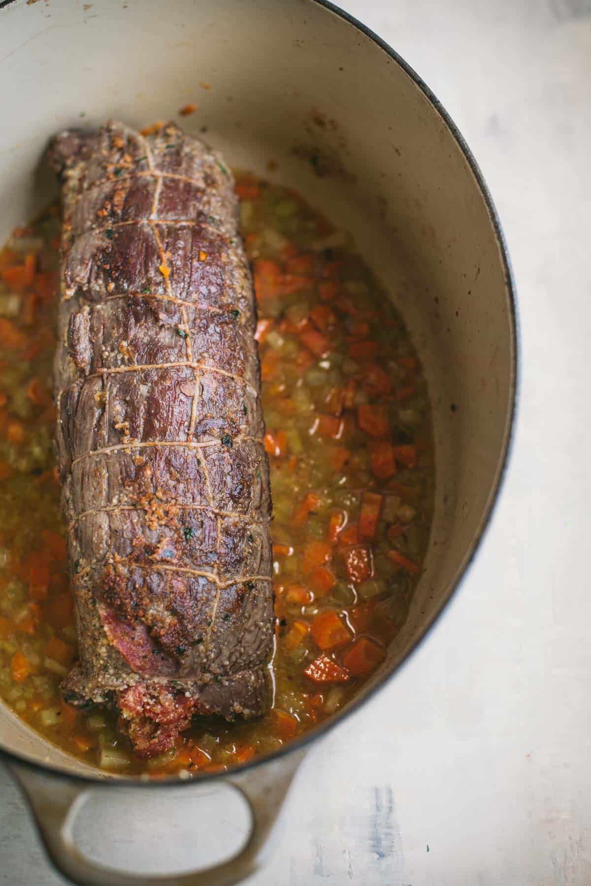 Inside the large white saucepan there is the beef braciole, the vegetables and wine.