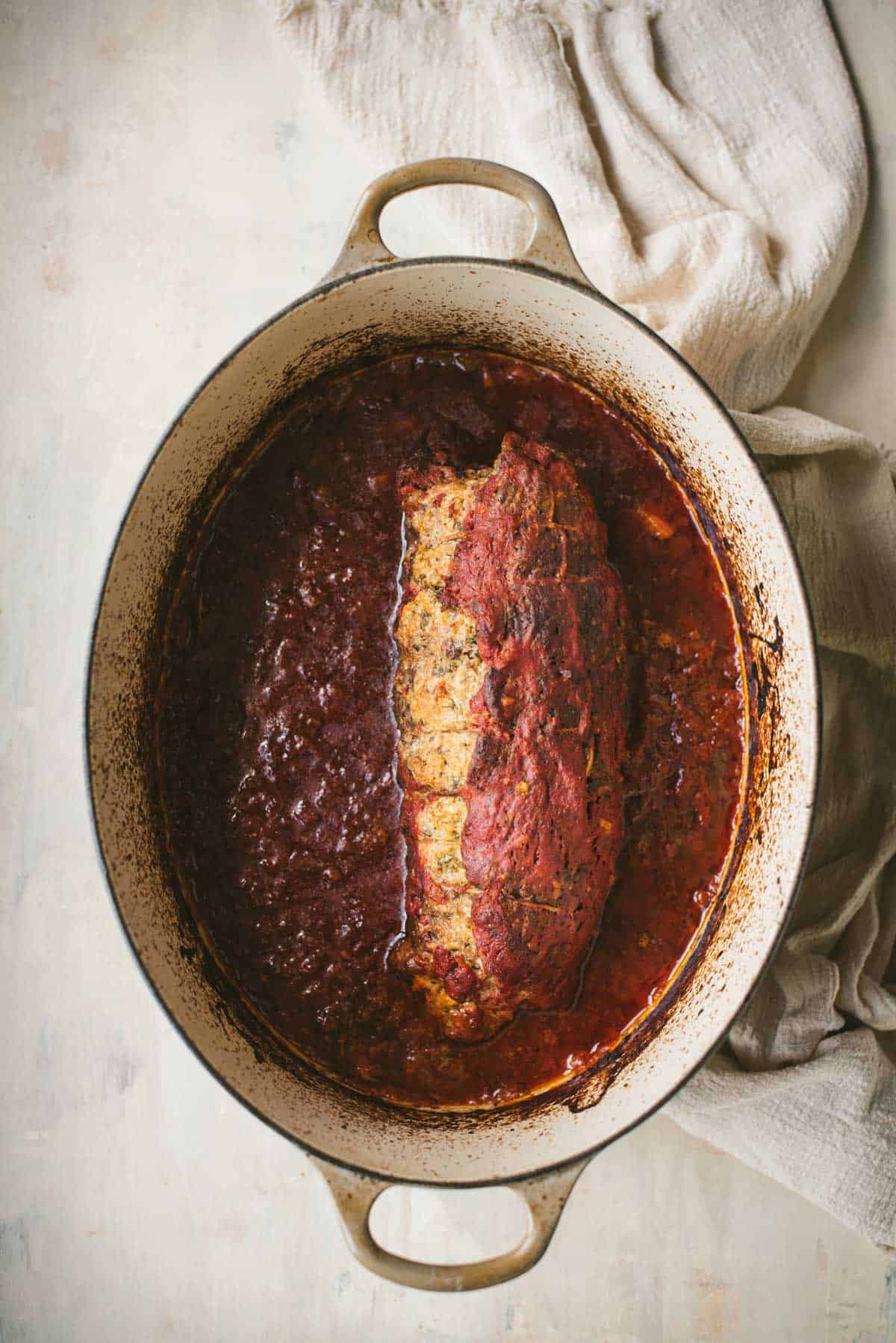 The dish has been cooked for 45 minutes in the large white saucepan. The braciole has shrunken in size and the bright red tomato sauce has gone much darker in color.