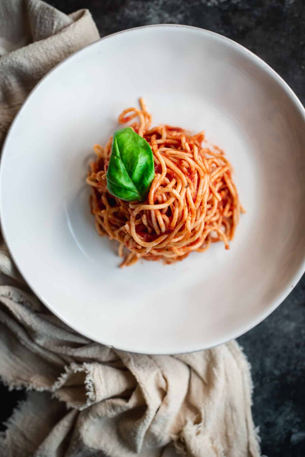 View from above of a tower of spaghetti mixed with easy homemade pasta sauce on a white plate and garnished with a fresh basil leaf.