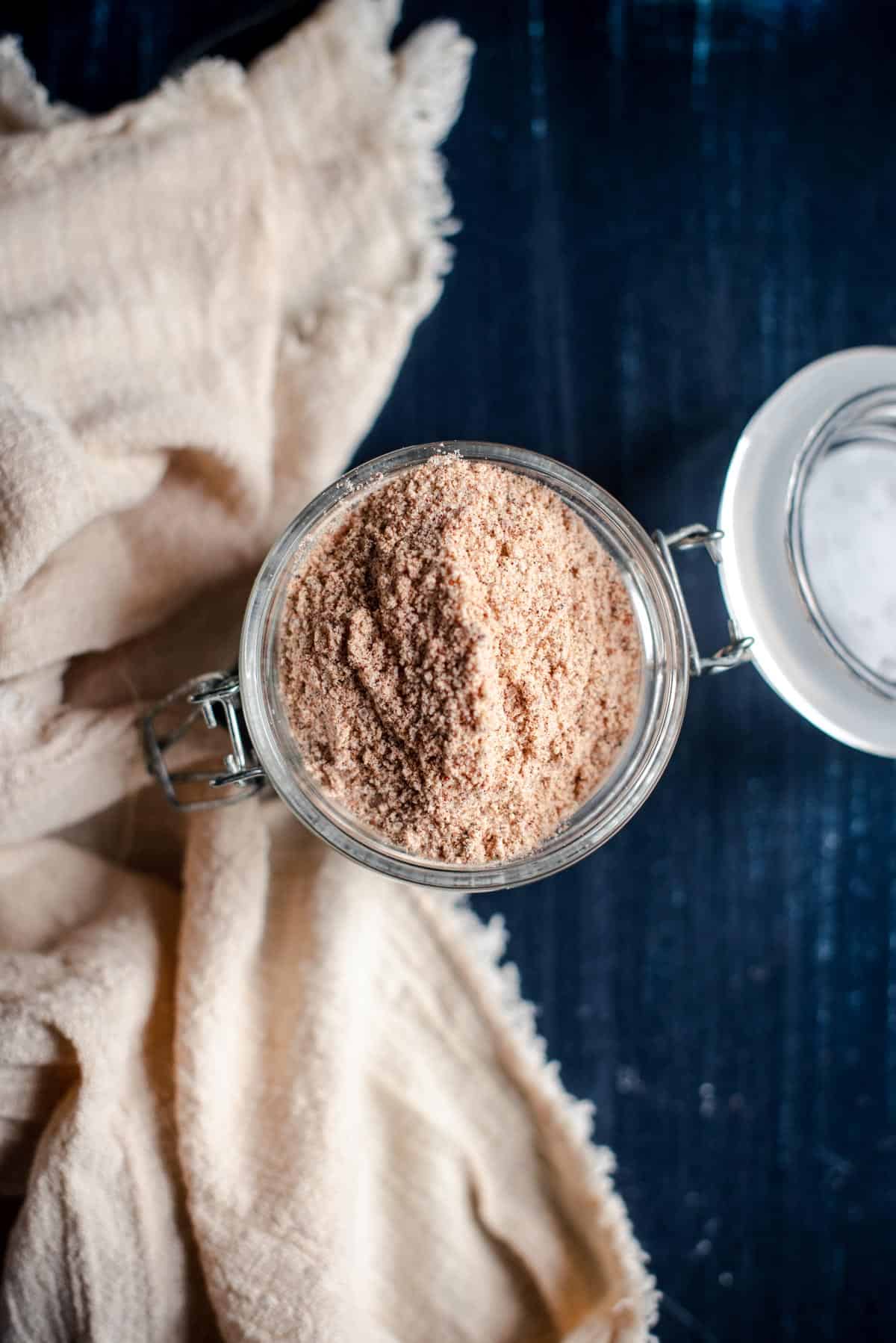 overhead image of seasoning in a flip top glass jar next to a cream colored linen napkin