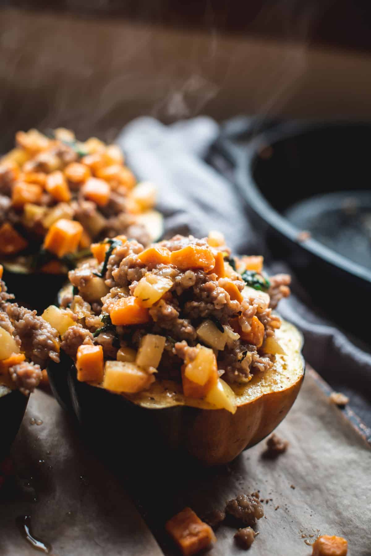 The finished result. This image shows 2 halves of acorn squash stuffed with the sausage stuffing mixture. The acorn squash are sitting on a lined baking tray, ready to be eaten.