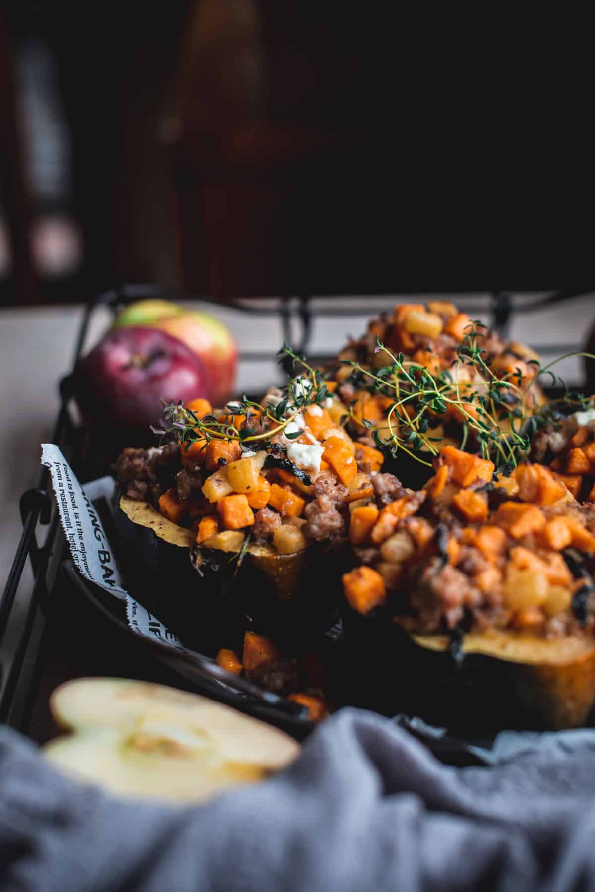 On a newspaper lined plate sit the stuffed acorns. They have been garnished with green herbs. Extra whole and halved apples leftover from the meal are left at the sides of the plate.