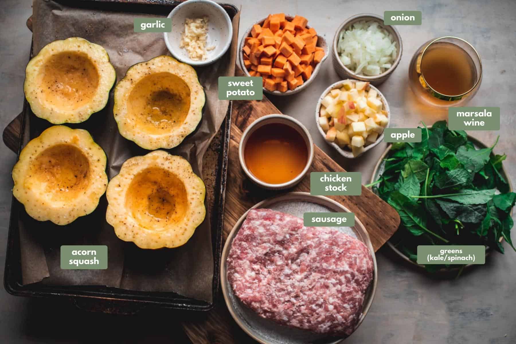 All the ingredients needeed to make sausage stuffed acorn squash. In a lined baking tray sit 4 half acorn squash and a ramekin dish filled with chopped garlic.  Next to  the tray is a bowl filled with cubed sweet potato, another bowl with chunks of apple and a bowl of chopped onions. A ramekin dish is filled with chicken stock and there is a glass of marsala wine. Finally there are 2 plates, 1 filled with greens like spinach and kale, and the other filled with sausage meat.