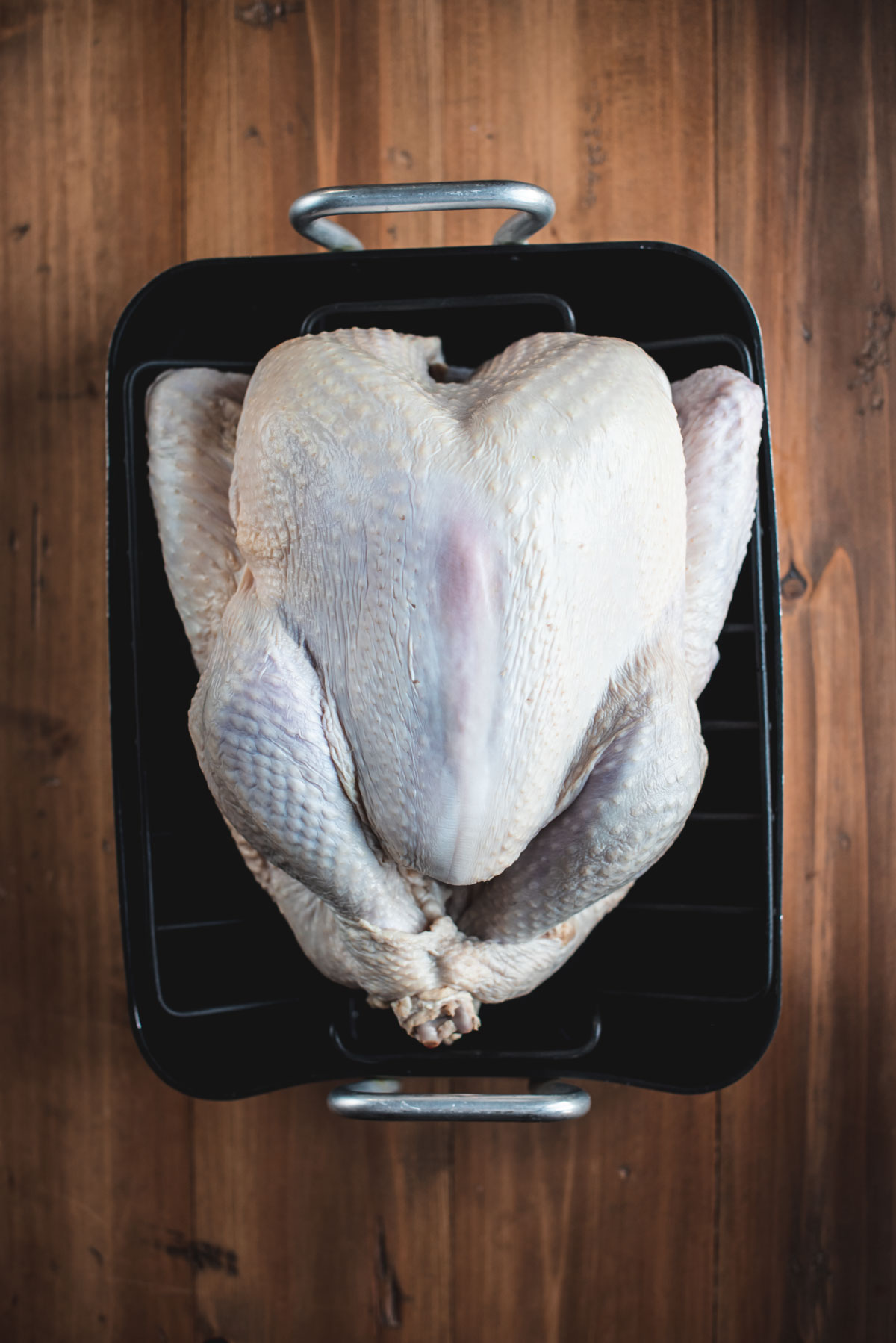 The turkey has been removed from the brining bag and placed onto a black baking tray.