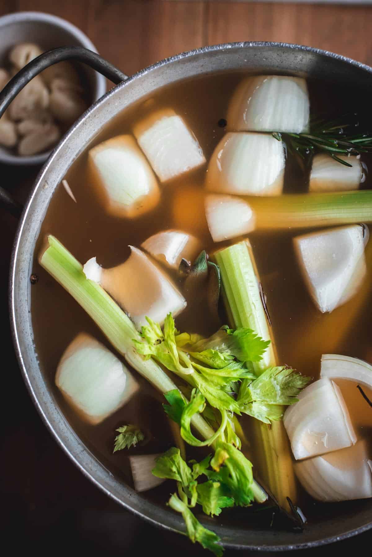 The apple cider, celery and onions have been added to the water and herb mixture in the stock pot. The small bowl of garlic is sitting next to the large stock pot.