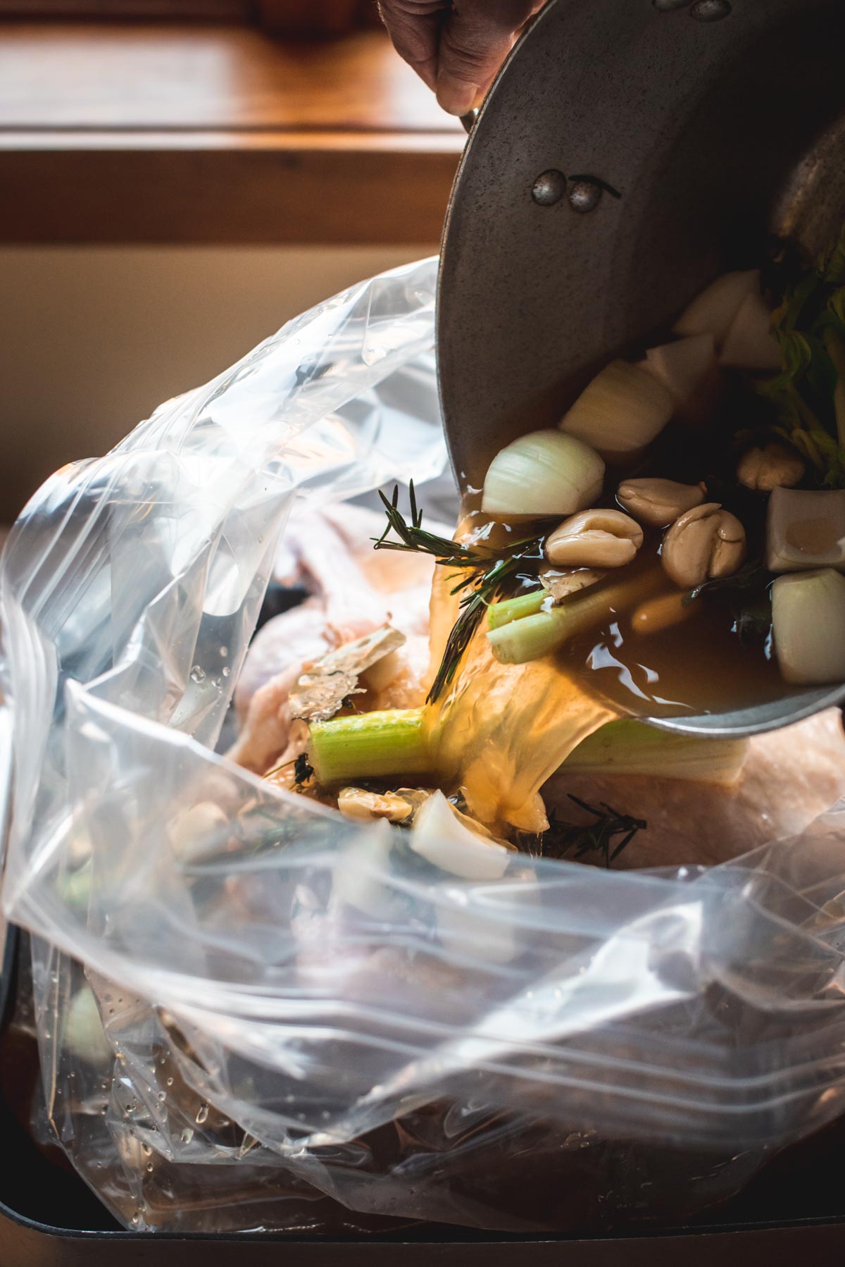 The turkey is inside the brining bag and the brining liquid is being carefully poured from the stockpot into the bag with the turkey.