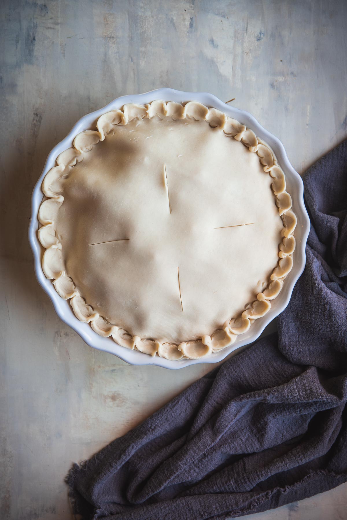 The pie has now been covered with the other piece of uncooked pastry. The edges have been neatly sealed and 4 line have been scored in the top of the pie, so steam can escape.