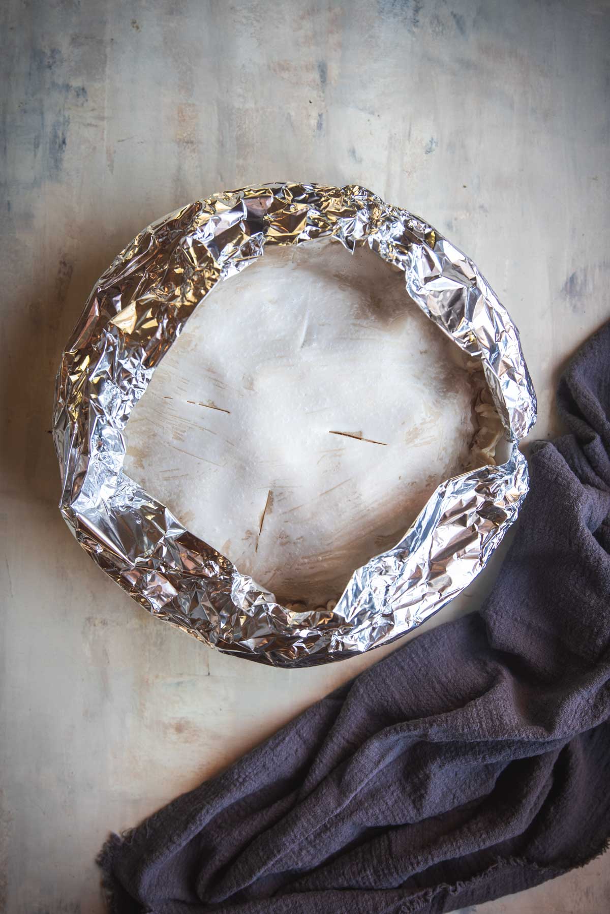 The pie has been brushed with egg was and you can see the faint lines it has left, there is tin foil covering the edges of the pie. It is now ready for the oven.