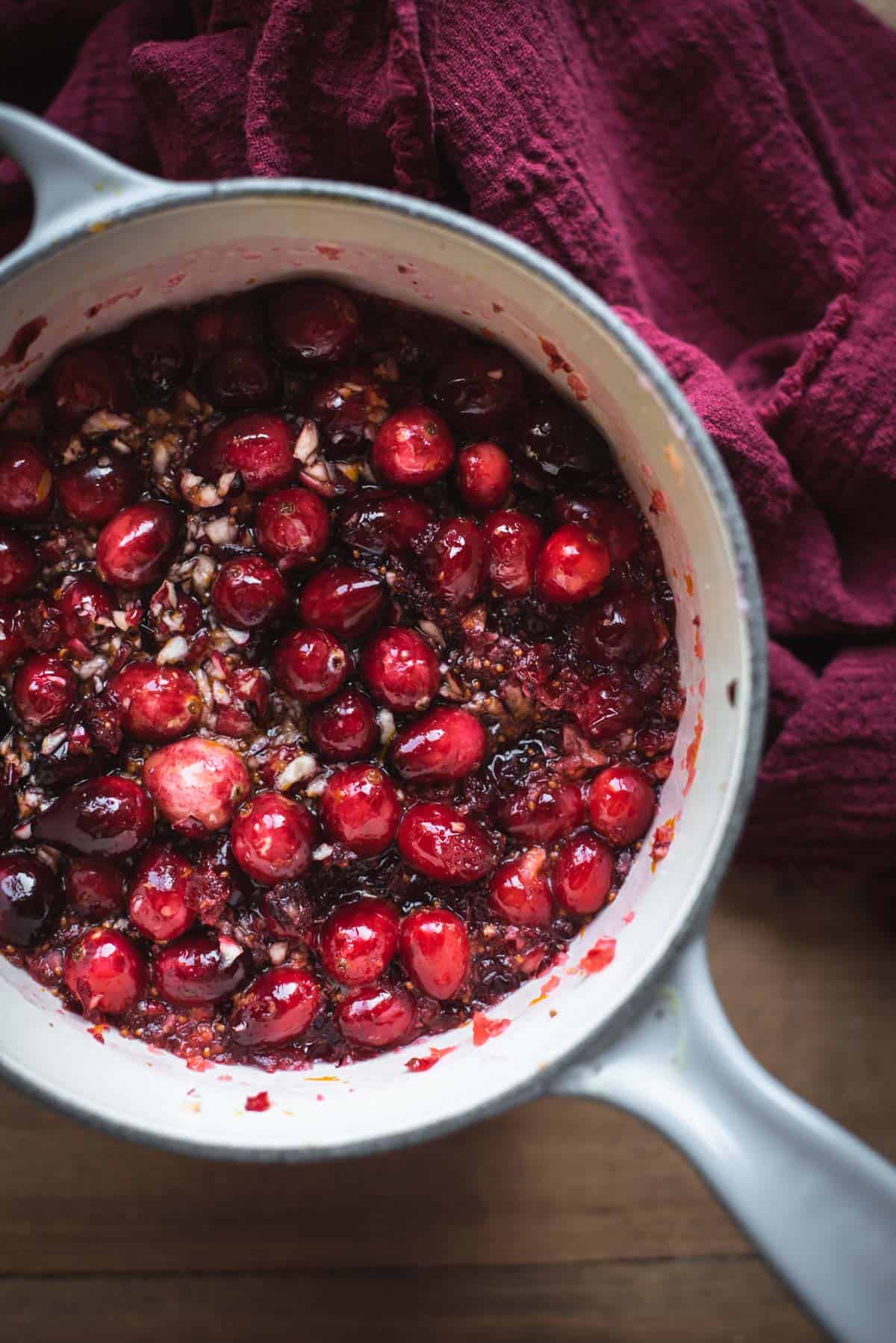 The mixture inside of the large pot has become thicker as it starts to bubble. There are cranberries sitting in thick red liquid as it cooks down.