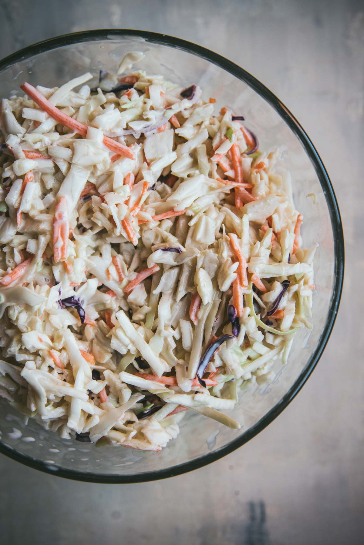A glass bowl is filled with coleslaw. There is cabbage and carrots inside.