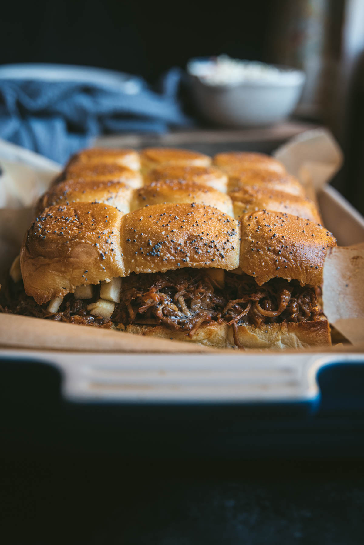 The top layer of the slider buns has now been added on top of the bun. 
The sliders have been build but not separated. A pack of 12 slider buns are used and sliced in half. They have been toasted and filled with pulled pork and coleslaw, They are now sitting on a sheet of baking paper on a baking tray.