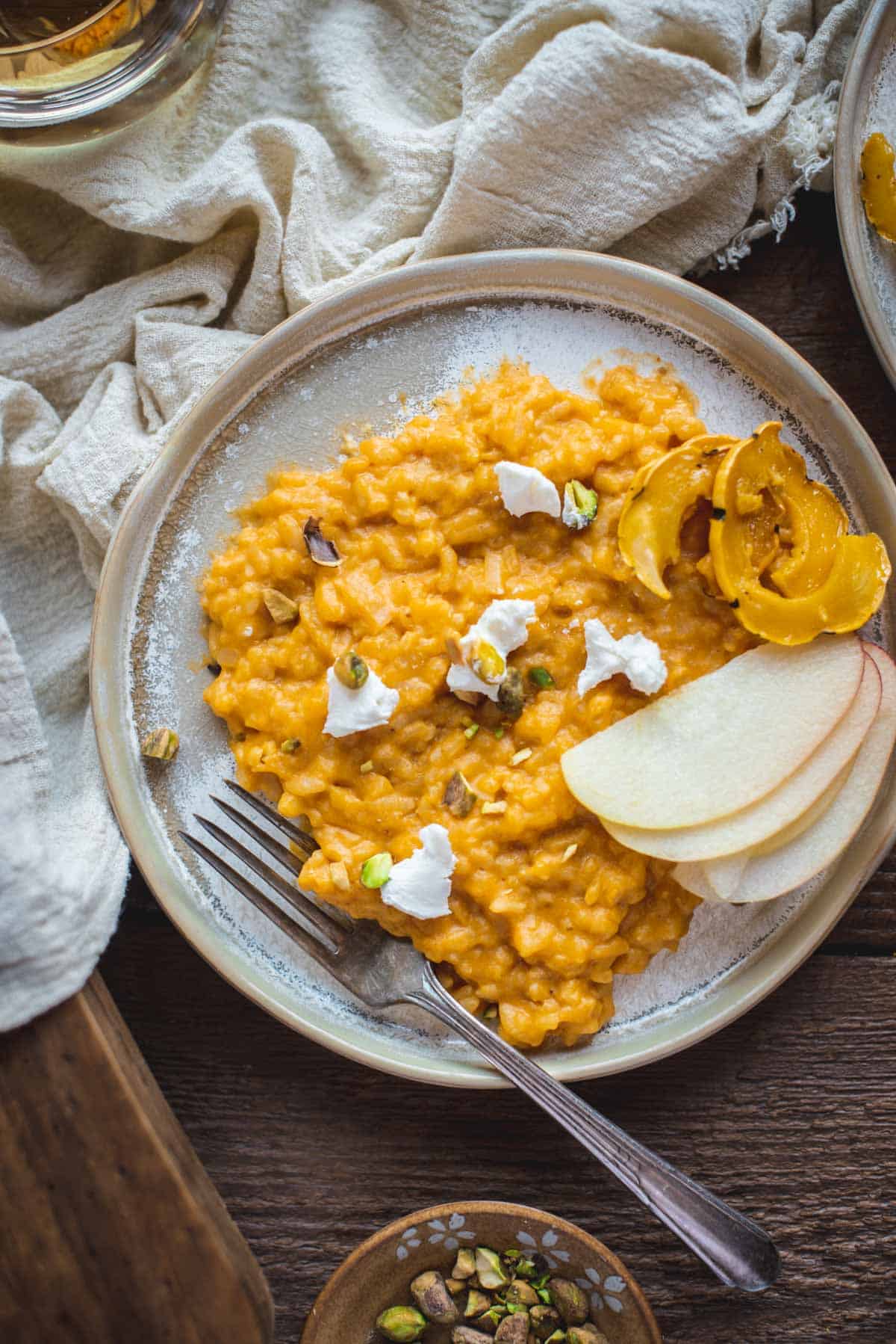 View from above of baked pumpkin risotto on a ceramic plate with a fork balanced on the side. There is chunks of soft goats cheese on top alongside some apple slices and pumpkin pieces.