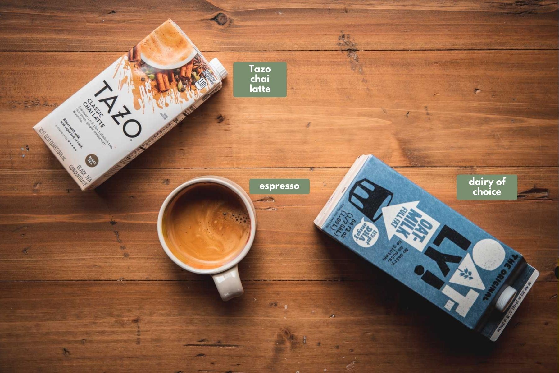 Overhead image of ingredients for making a dirt chai latte on top of a wooden board.  The ingredients are Tazo chai latte, espresso, and oat milk.