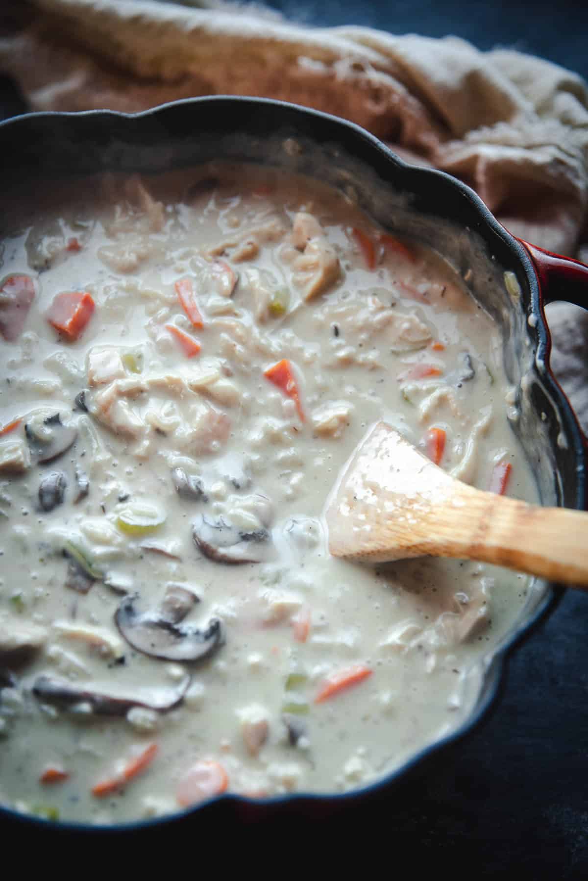 The soup has changed to a pale white  color with the addition of heavy cream The wooden spoon has incorporated all the ingredients and it looks ready to serve.