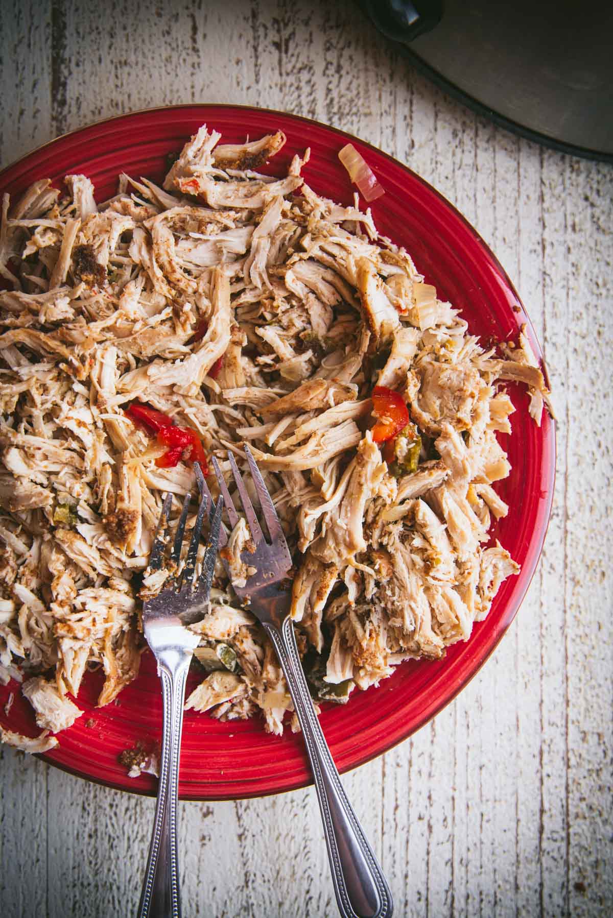 The chicken has been shredded between 2 forks and placed on a red plate with the 2 forks sitting on top.