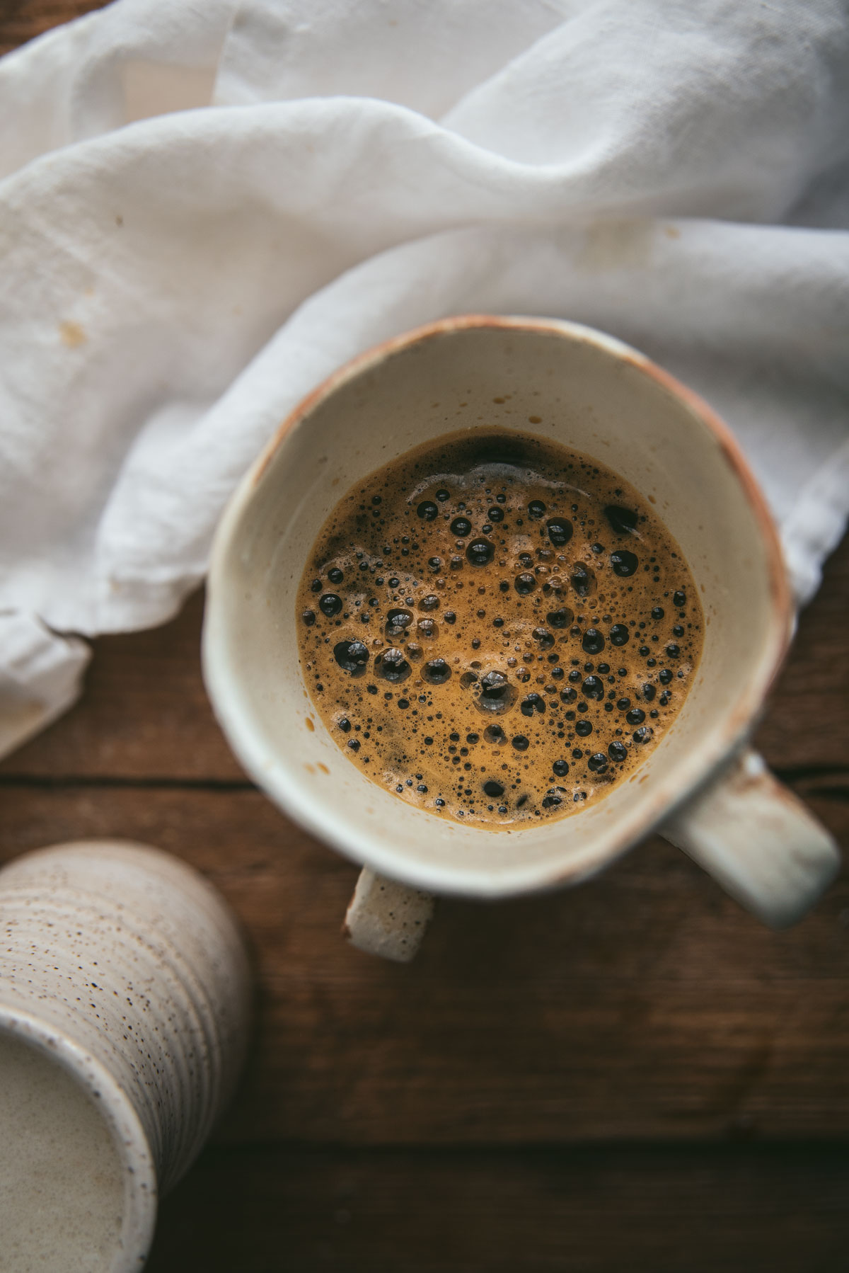 close up image of fresh brewed espresso in a white mug set on top of a wooden background with a white linen napkin behind the mug.