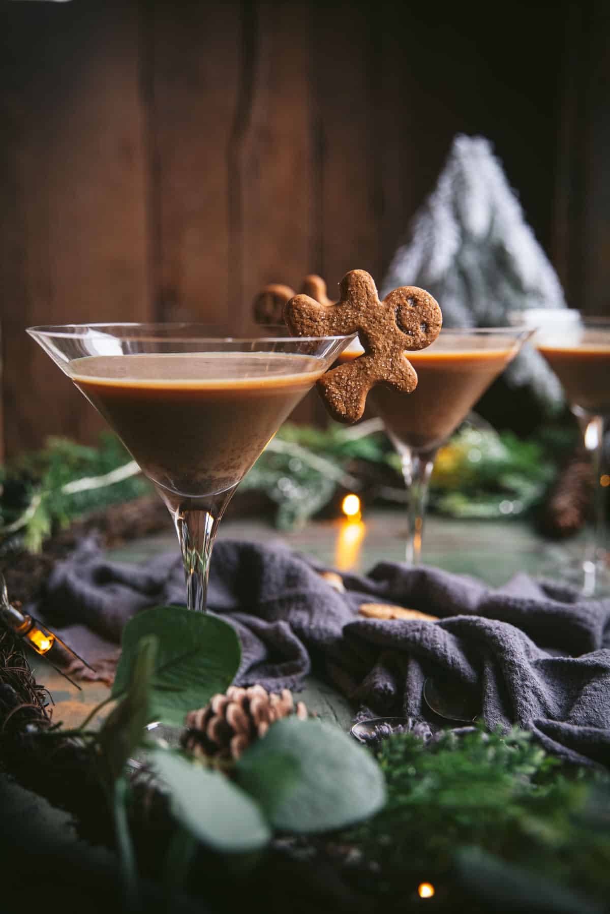 gingerbread cookie person hanging off a martini glass filled with gingerbread espresso martini.  Two additional martinis are in the background.