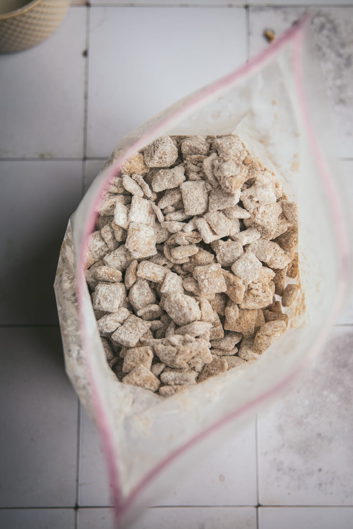 Overhead image of the finished puppy chow inside the plastic zip bag.  It has been coated with the powdered sugar and has a light brown color dusted with white powdered sugar.